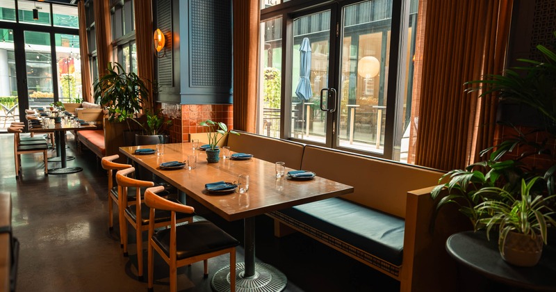Sunlit dining area with large windows, warm wood seating