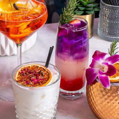 Colorful cocktails garnished with citrus, rosemary, and an orchid.