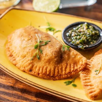 Two golden-brown empanadas served on a yellow plate with green sauce.