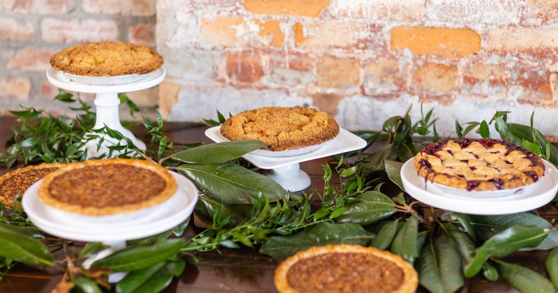 Assorted pies displayed on stands on a table decorated with greenery