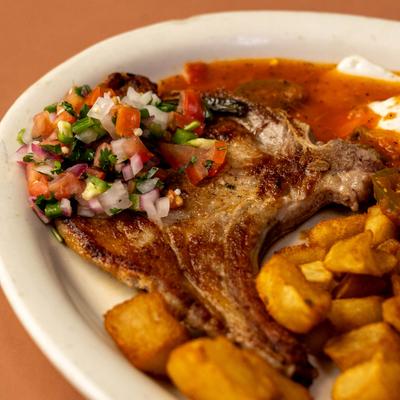 Pork chop topped with pico de gallo and served with roasted potatoes, close-up.