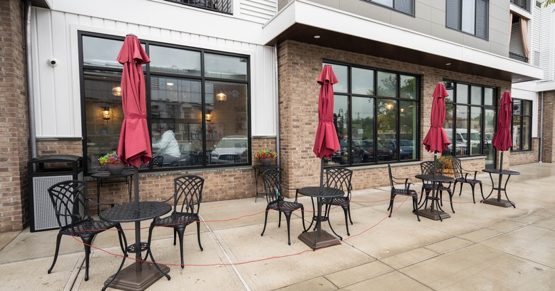 Outdoor seating area with tables, chairs, and red umbrellas outside a building