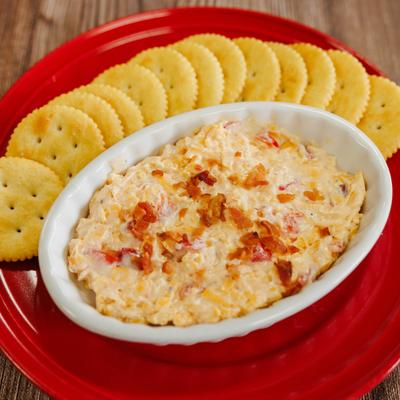 Pimento cheese spread garnished with bacon bits, served with crackers.
