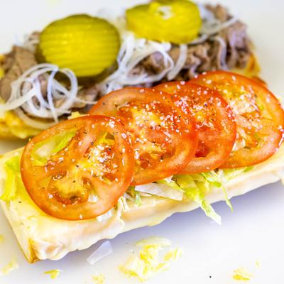 Open roast beef sandwich with tomato, lettuce, red onion, and pickles.