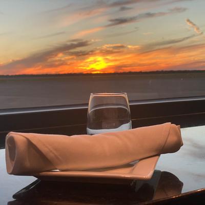 A napkin and glass on a table by a window with the sunset sky in the background.
