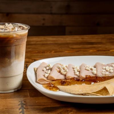Goat cheese and turkey crepe served on the table alongside cup of iced coffee.