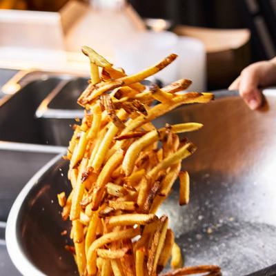 French fries being tossed in a metal bowl.