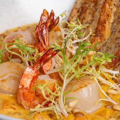 Shrimp and scallops in a creamy orange sauce with pine nuts and bread slices.