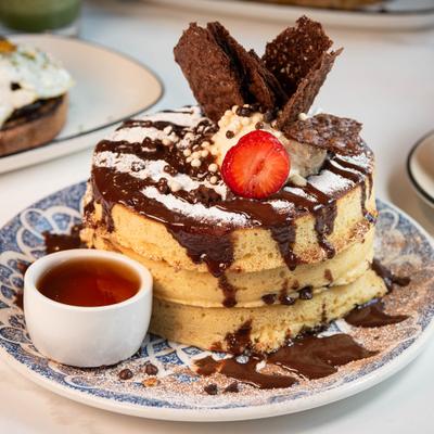 Thick fluffy pancakes topped with chocolate drizzle, crisps, and a sliced strawberry.