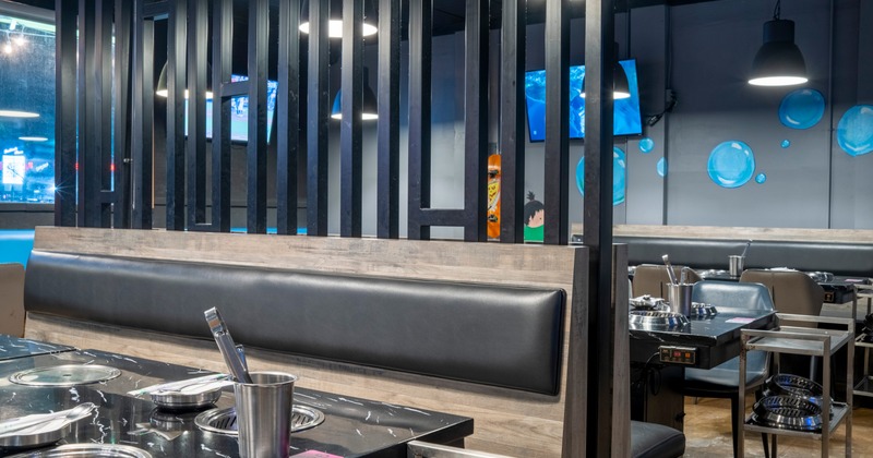 Interior of a modern restaurant with booths, black marble tables with grills, and decorative wall elements