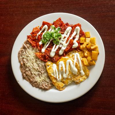 Tortilla chips smothered in red salsa, fried eggs, potatoes, sour cream, and beans.