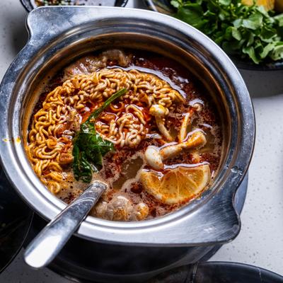 Instant noodle hot pot with mushrooms, leafy greens, and a slice of lemon.