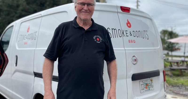 An employee posing in front of Smoke and Donuts catering van