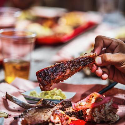 A hand lifting a seasoned rib above a plate of barbecued meat.