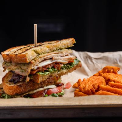 Stacked club-style sandwich served with a side of crispy sweet potato fries.