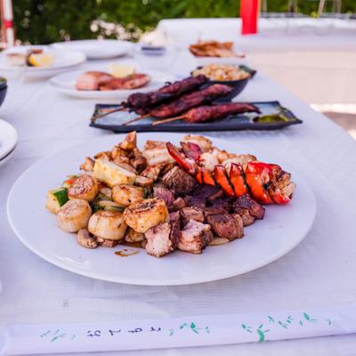 A plate of assorted seafood and meats on an outdoor table with other dishes.