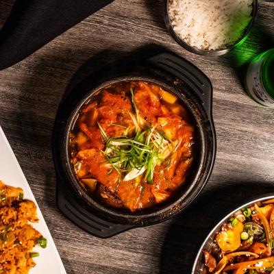 Spicy, boiling Korean kimchi stew served with white rice in a clay pot.