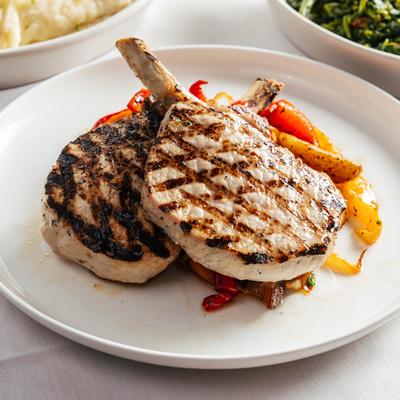 Grilled Berkshire Loin Pork Chops, served with potatoes, onions, and peppers.