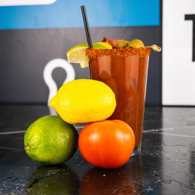 Bloody Mary topped with edible garnishes and surrounded by fresh ingredients.