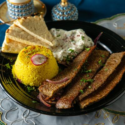 Gyro platter with sides of couscous, a white sauce, and pieces of pita.