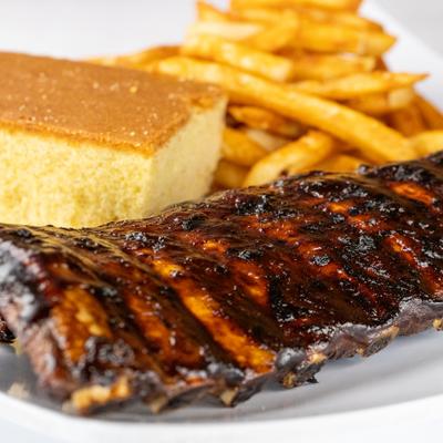 Baby back ribs served with a slice of cornbread and French fries.