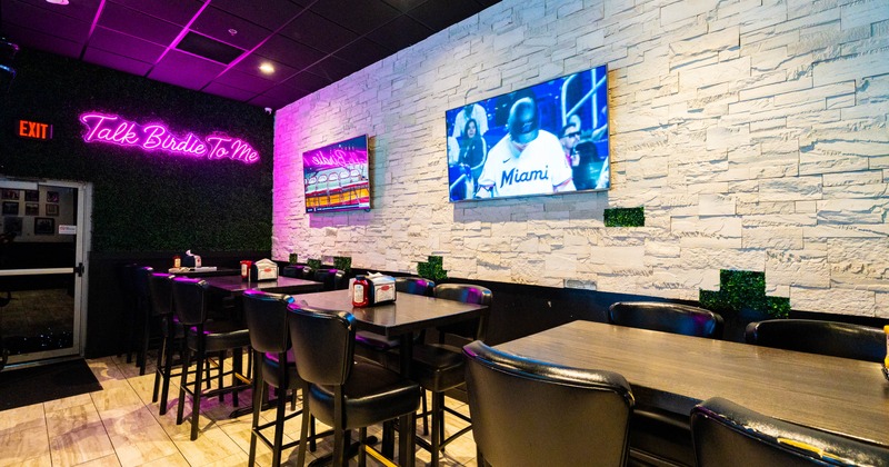 Sports bar with black tables and chairs, purple lighting, and televisions
