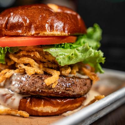 Beer Cheeseburger with crispy onion straws, lettuce, and tomato on a pretzel bun.