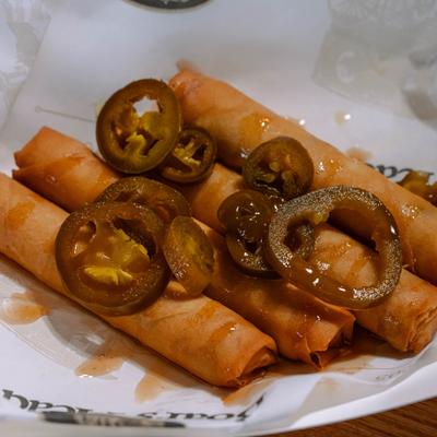 Close-up of crispy egg rolls topped with pickled jalapenos and sweet and sour sauce.