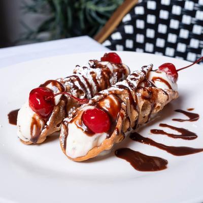Two cream-filled cannoli topped with chocolate drizzle and cherries on a white plate.
