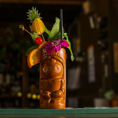 A richly garnished drink in a tiki cup, sitting on the bar counter.