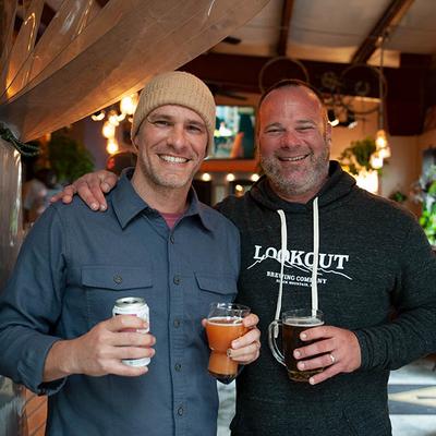 Two people holding drinks and smiling indoors.