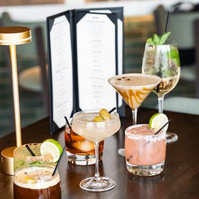 Table setting with an assortment of cocktails, a menu card, and a gold table lamp.