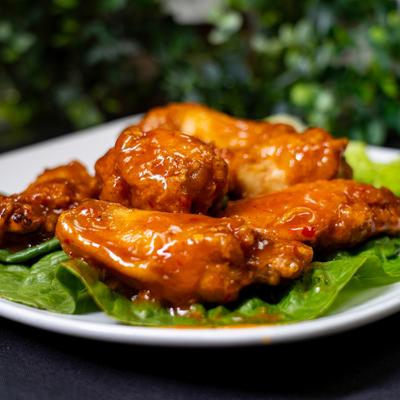 Wings covered in sauce, served pver lettuce leaves.