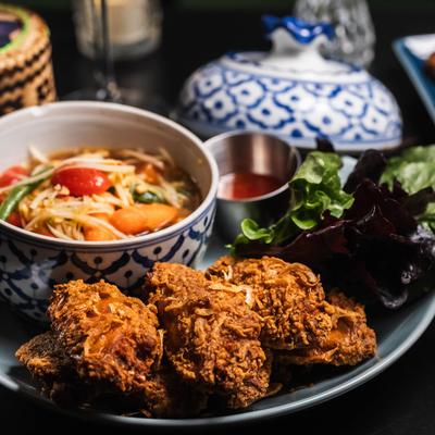 Crispy fried chicken accompanied by spicy papaya salad, dipping sauce, and fresh greens.