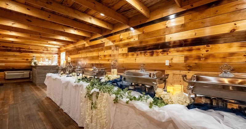 Interior, long  white cloth buffet table with stylish catering  chafers, wood coated walls