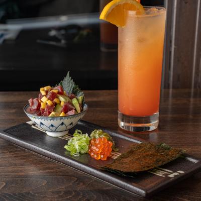 Tuna poke bowl with avocado and mango served with roe, seaweed, and orange cocktail.