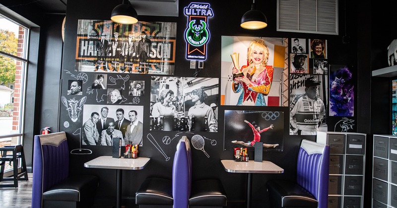 Two dining tables by the wall with photos of famous persons