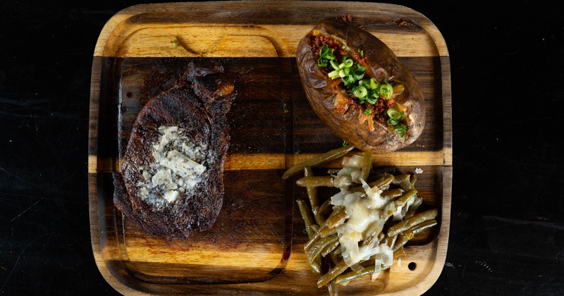 Buttered steak served with a loaded baked potato and green beans