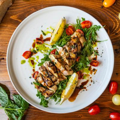 Grilled and sliced chicken with arugula, tomatoes, and lemon, top view.