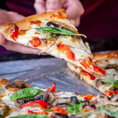 Veggie pizza slice held above the pizza plate, close up.