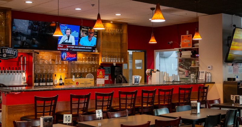 Interior, sushi bar, stools in line, screen tv above, drink rack behind
