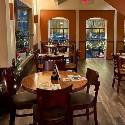 Row of round wooden tables inside a restaurant with arched windows.
