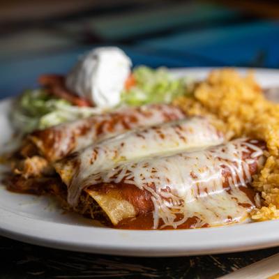 Enchiladas covered in mole sauce, served with salad, sour cream, rice and beans