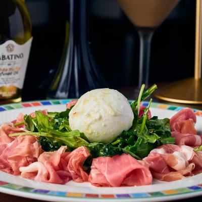 Burrata cheese on arugula salad surrounded by prosciutto cured meat.