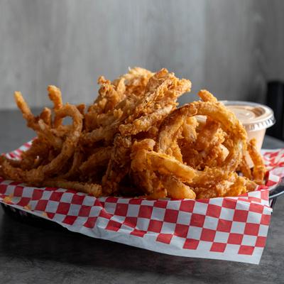 Birdies nest onion strings in a basket with a cup of dipping sauce.