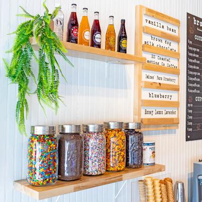 Wooden shelves display colorful glass soda bottles and bright candy jars against a white wall.