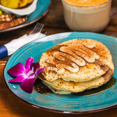 Tiramisu Pancakes topped with sauce and groung cocoa, garnished with a flower.