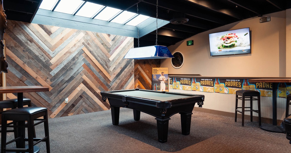 A room with a pool table, bar tables and stools, and a TV mounted on a wall