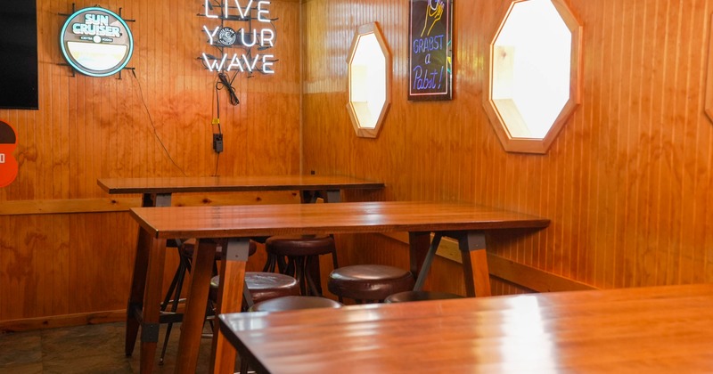 Interior of a bar with wooden walls, high tables, and neon signs