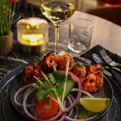 Chicken Tikka served with sliced red onions, a wedge of lime, cucumber, and herbs.